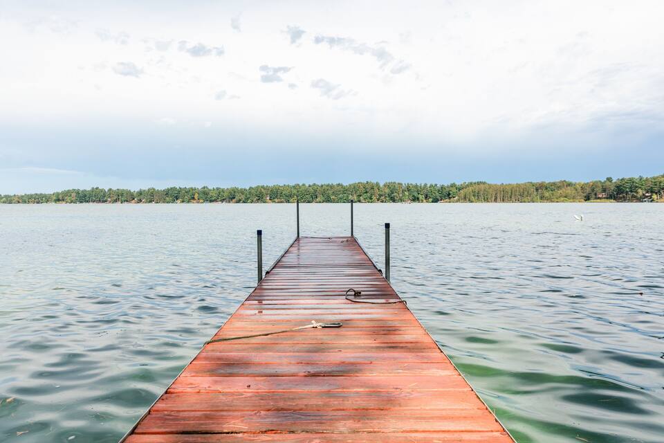 A wooden pier extending into calm water with a forested shoreline in the background.
