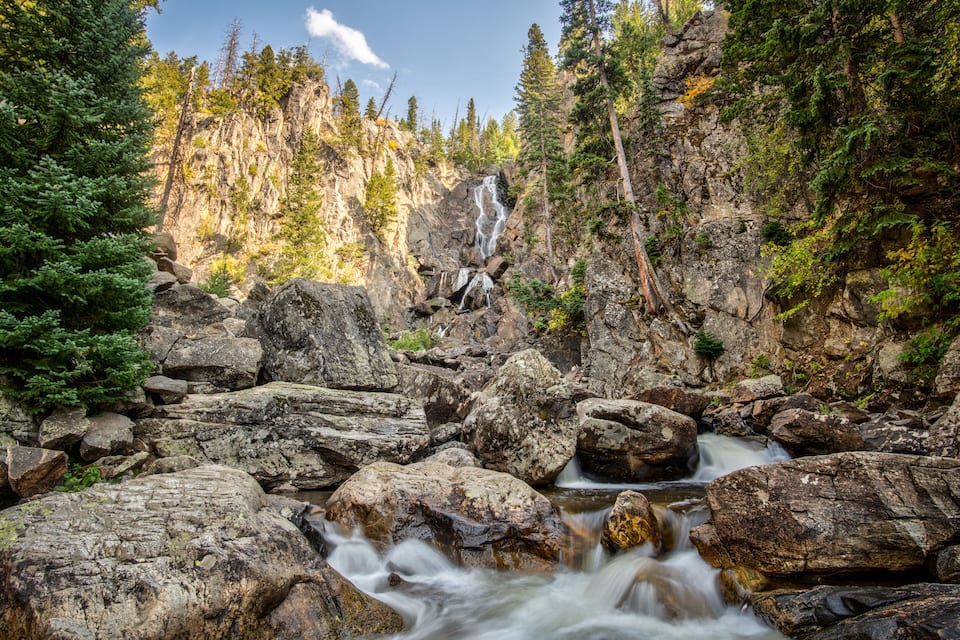 A waterfall in a forested area with large rocks and trees.