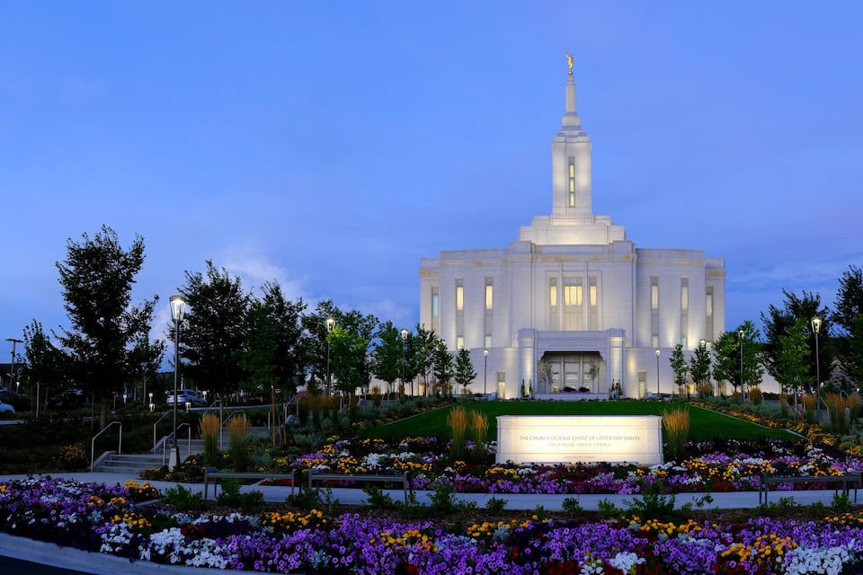 Una iglesia con una aguja alta, rodeada de un jardín con flores coloridas.