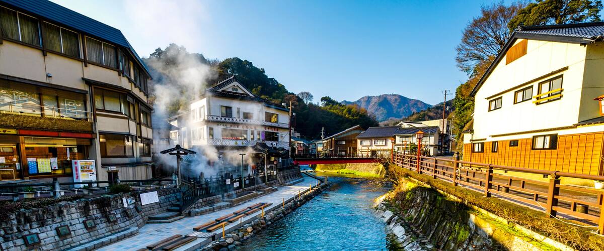 A river flowing through a town with traditional buildings, a bridge, and mountains in the background.