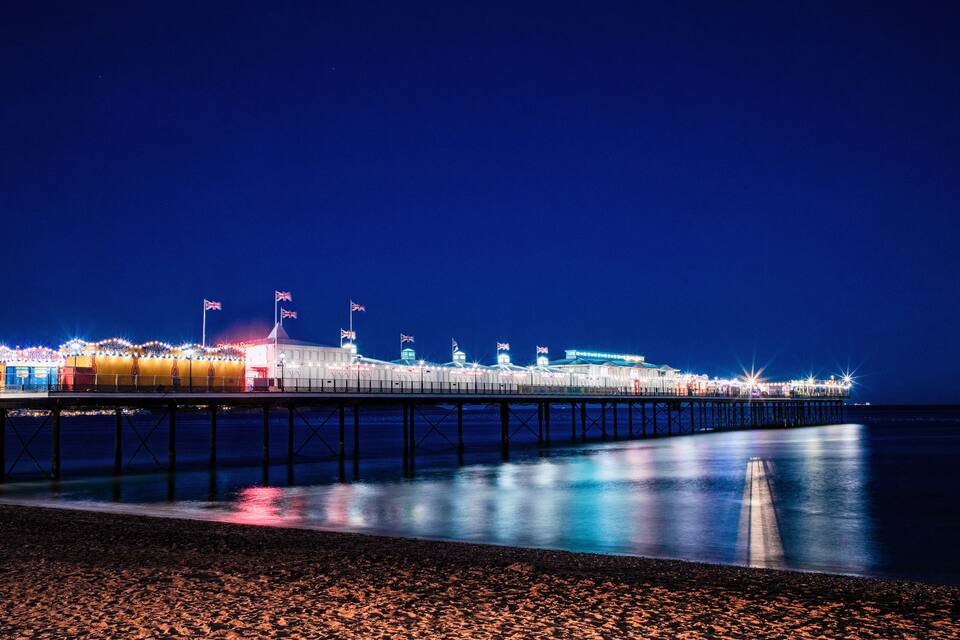 A pier at night with illuminated buildings and flags.