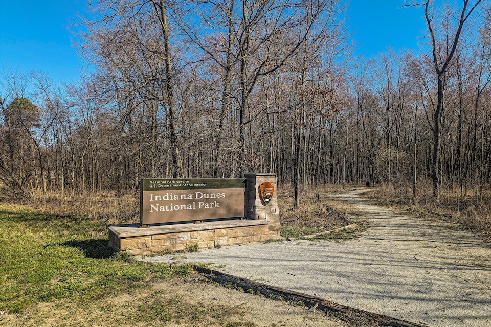 A sign for Indiana Dunes National Park with a gravel path leading through a wooded area.