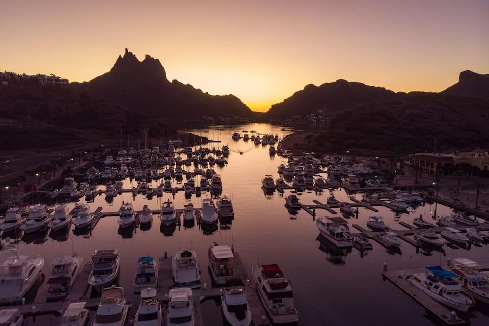 Un puerto deportivo al atardecer con barcos amarrados y montañas al fondo.