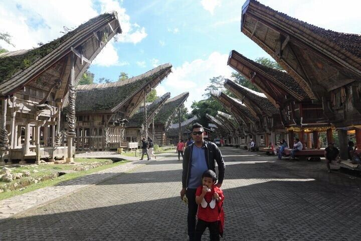 A traditional wooden structure with a curved roof, a cobblestone street, and a person holding a child.