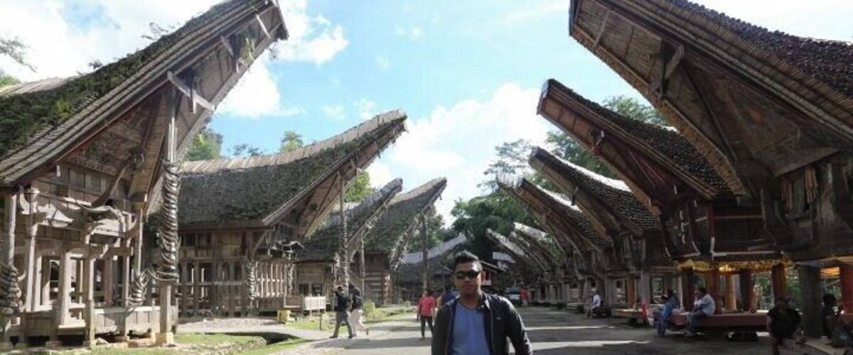 A traditional wooden structure with a curved roof, a cobblestone street, and a person holding a child.