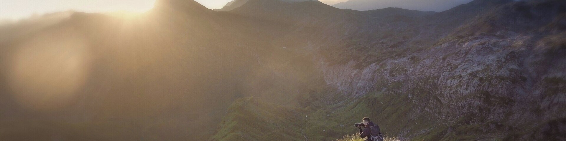 Una persona de pie sobre una colina cubierta de hierba, con montañas al fondo.