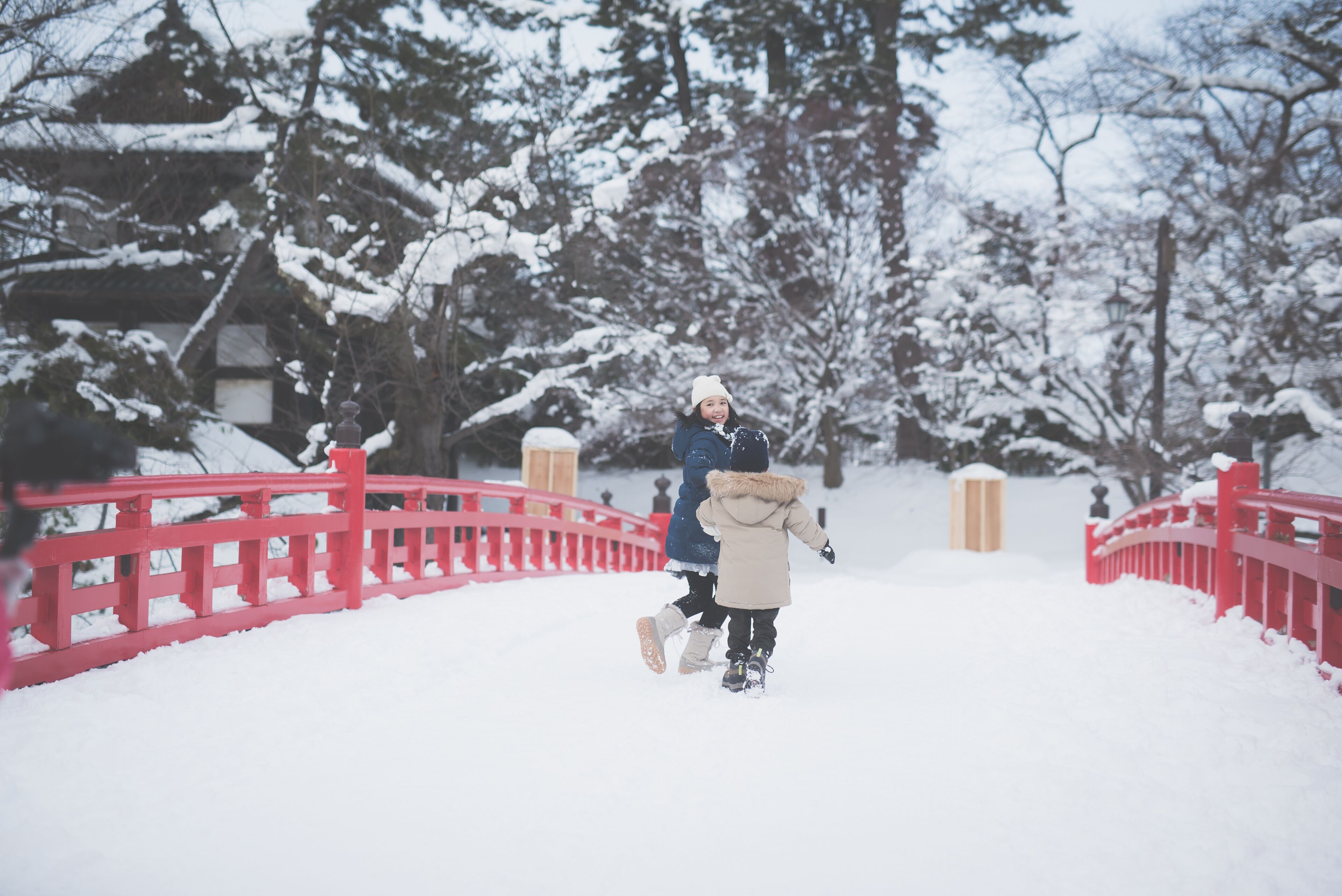 Paisagem nevada com uma ponte vermelha, árvores cobertas de neve e uma pessoa vestida para o inverno.