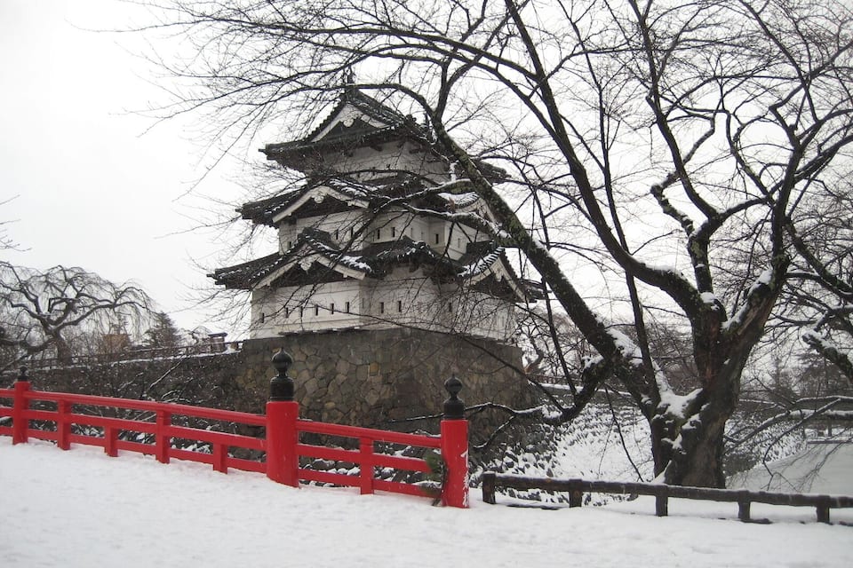 A traditional Japanese castle with a red fence in the foreground.