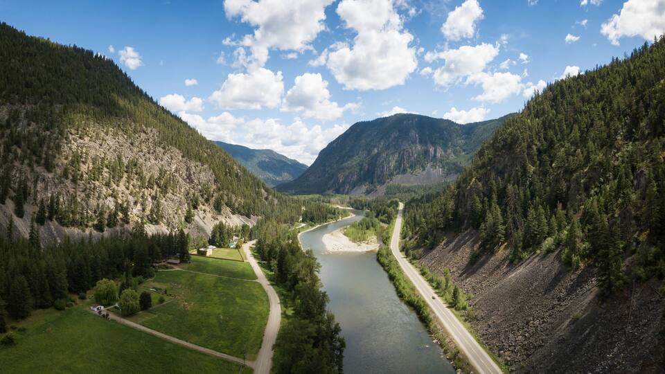 A river winding through a valley flanked by forested mountains under a partly cloudy sky.