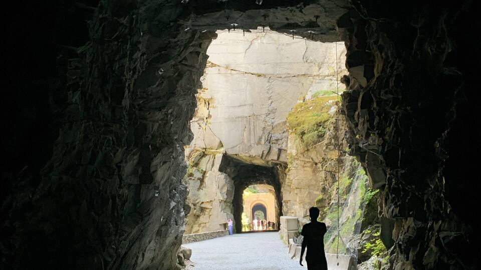 A person standing in a cave with a tunnel in the background.