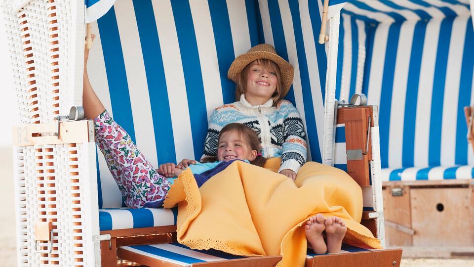 A beachside lounge chair with a striped awning, a wooden side table, and a beach umbrella.