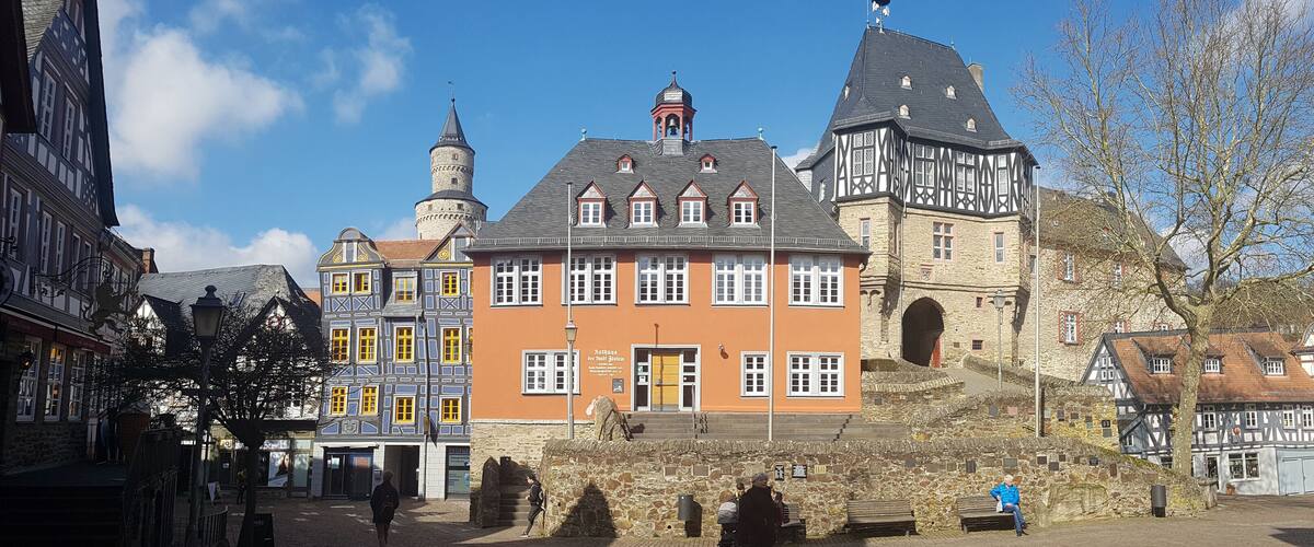 A historic town square with a prominent building featuring a tower and a large arched entrance.