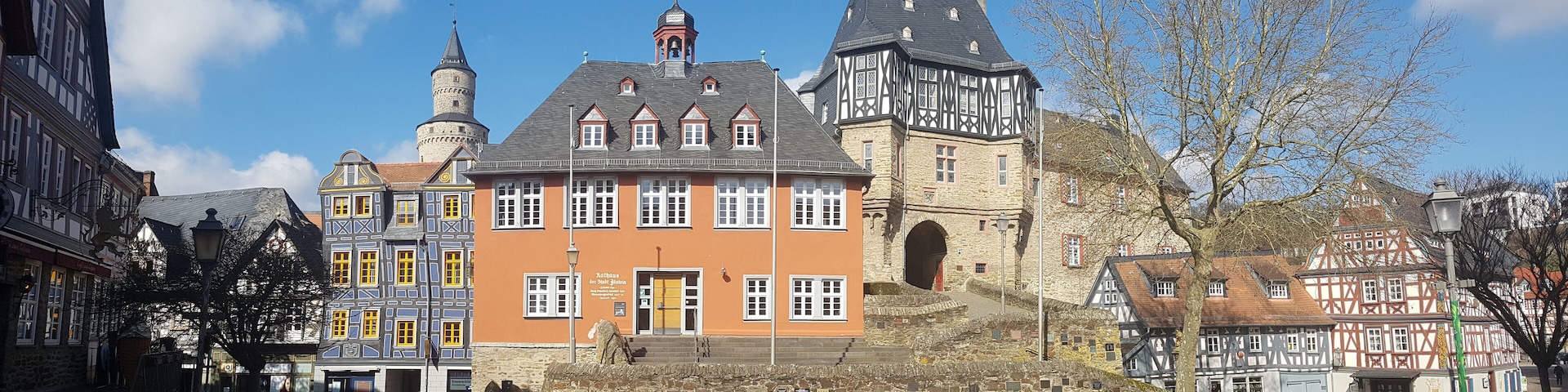A historic town square with a prominent building featuring a tower and a large arched entrance.