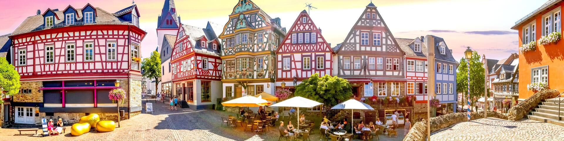 A cobblestone square with traditional half-timbered buildings, outdoor seating, and a clear sky.