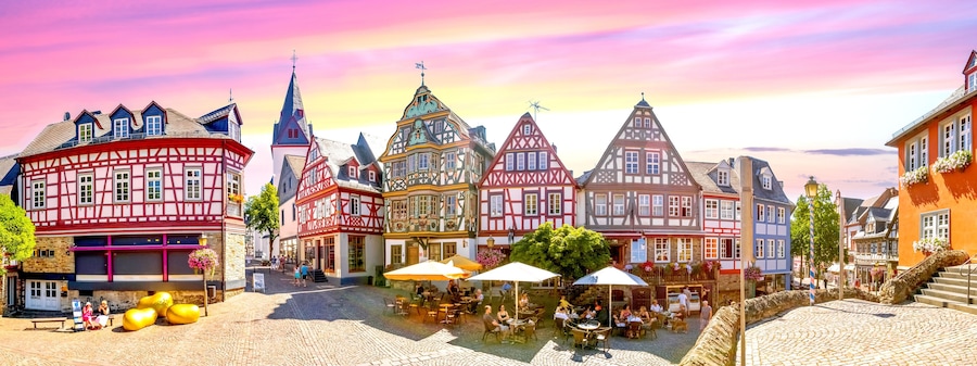 Ein Kopfsteinpflasterplatz mit traditionellen Fachwerkhäusern, Außenbestuhlung und blauem Himmel.