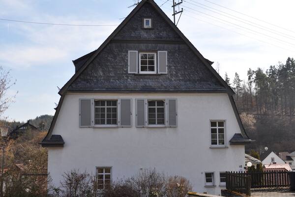 Ein weißes Haus mit dunklem Dach und weißen Fensterläden, umgeben von einem Rasen und einem Holzzaun.