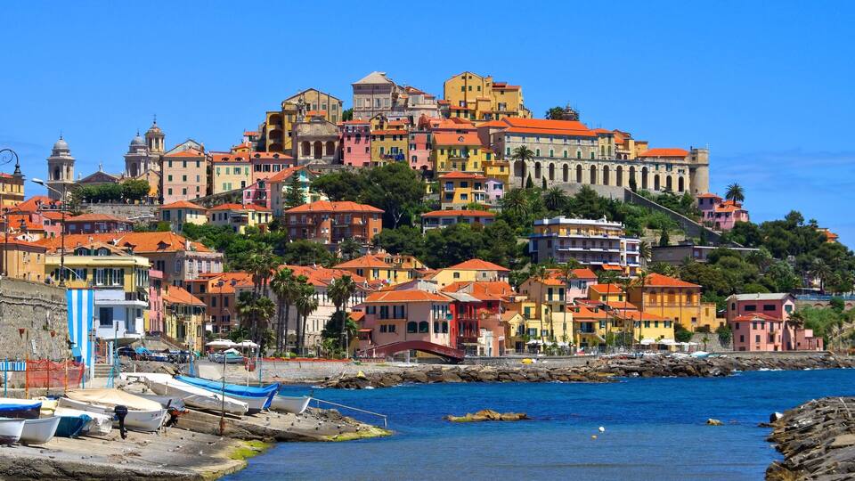 A coastal town with colorful buildings, a rocky shoreline, and boats docked along the pier.