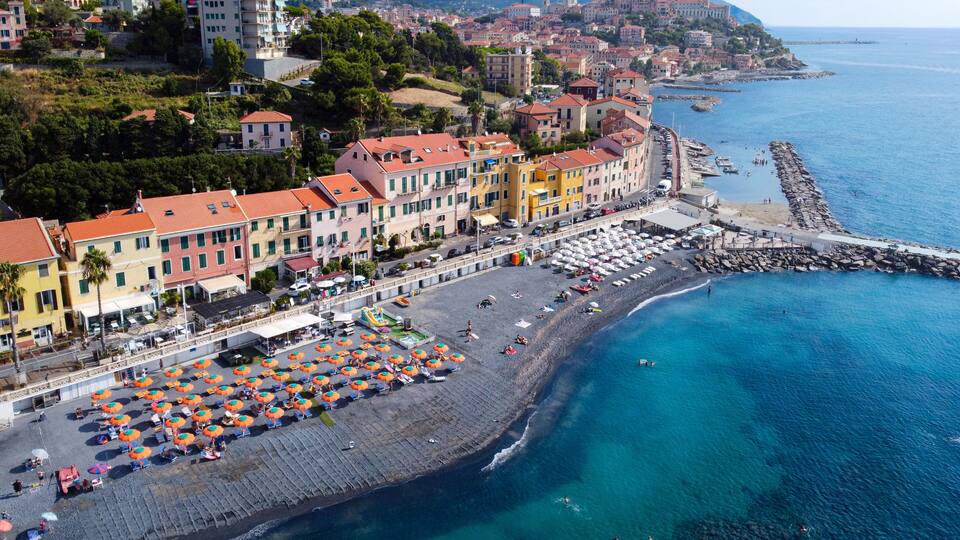 A coastal town with colorful buildings, a sandy beach, and a rocky breakwater.