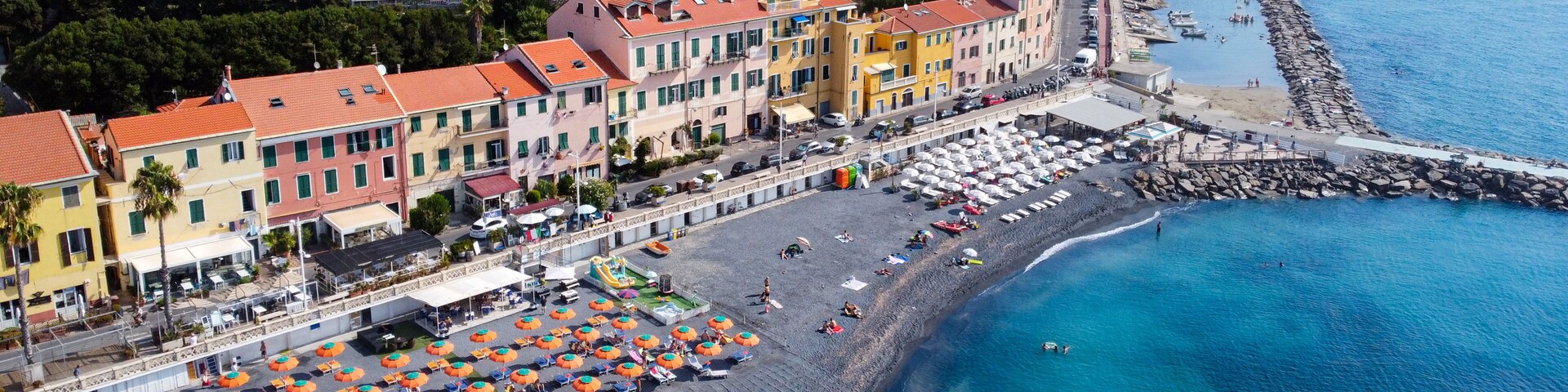 Aerial view of the coastal town featuring colorful buildings and a dark sand beach with orange umbrellas along the turquoise sea in Imperia, Liguria, Italy.