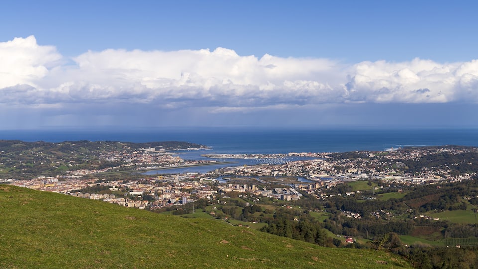 A coastal city with a river, green hills, and a clear blue sky.