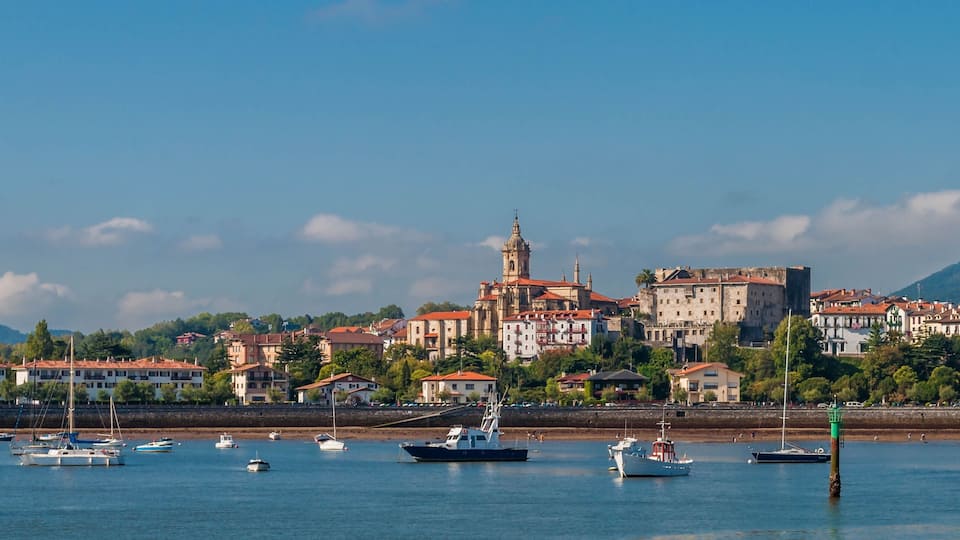 A coastal town with historic buildings, a prominent church tower, and a marina with boats.