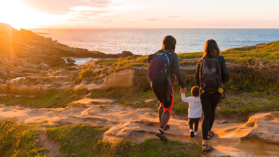 A family walking on a rocky coastal path during sunset.