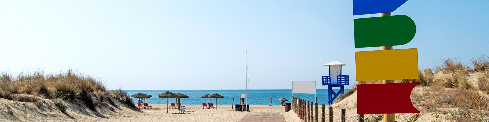 Una pasarela de madera que conduce a una playa con sombrillas y sillas reclinables.