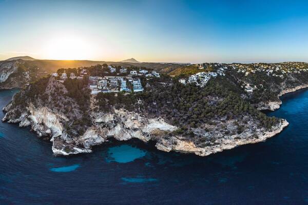 Vista aérea de una isla costera con edificios, terreno rocoso y aguas azul cristalino.