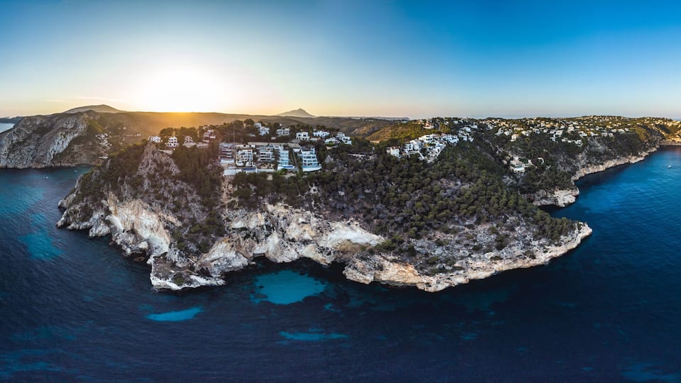 An aerial view of a coastal island with buildings, rocky terrain, and clear blue waters.