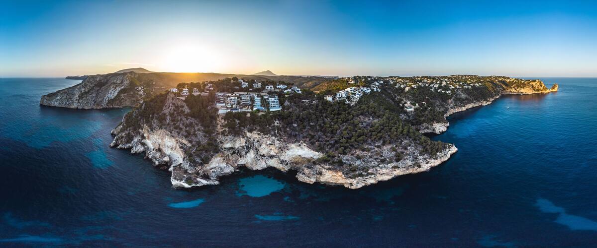 An aerial view of a coastal island with buildings, rocky terrain, and clear blue waters.