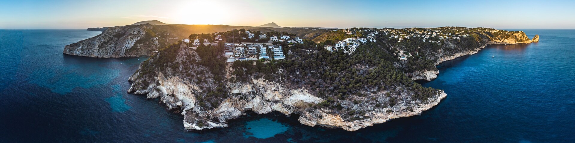 An aerial view of a coastal island with buildings, rocky terrain, and clear blue waters.