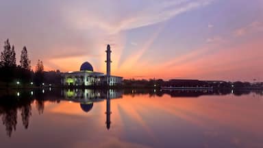 Una mezquita con un minarete alto y una cúpula, reflejada en un cuerpo de agua tranquilo al atardecer.