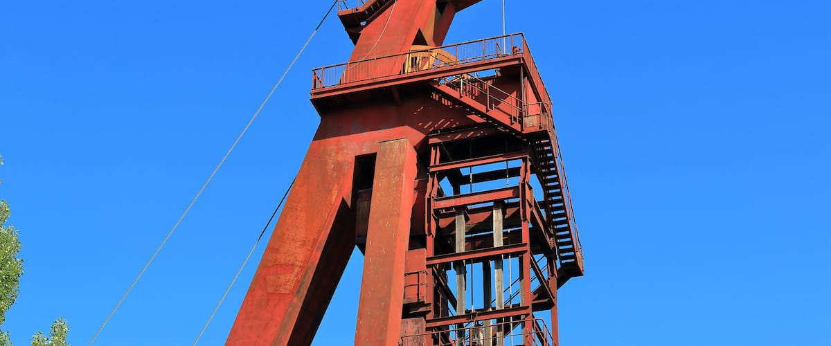A tall red metal structure with a staircase and railings against a clear blue sky.