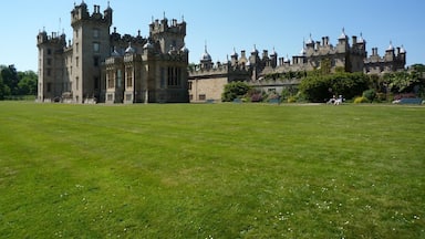 Um castelo grande e histórico com várias torres e ameias, rodeado por um jardim bem cuidado.