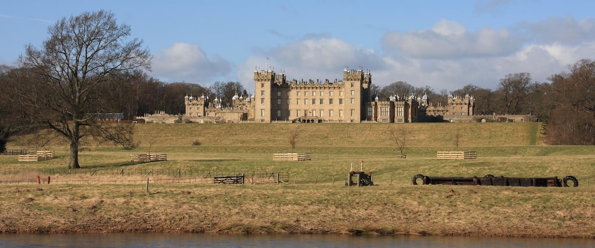 A large castle with multiple towers, surrounded by a grassy field and a body of water.