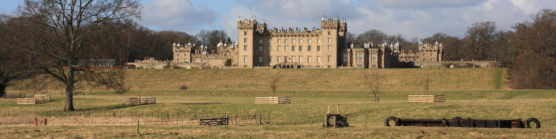 A large castle with multiple towers, surrounded by a grassy field and a body of water.