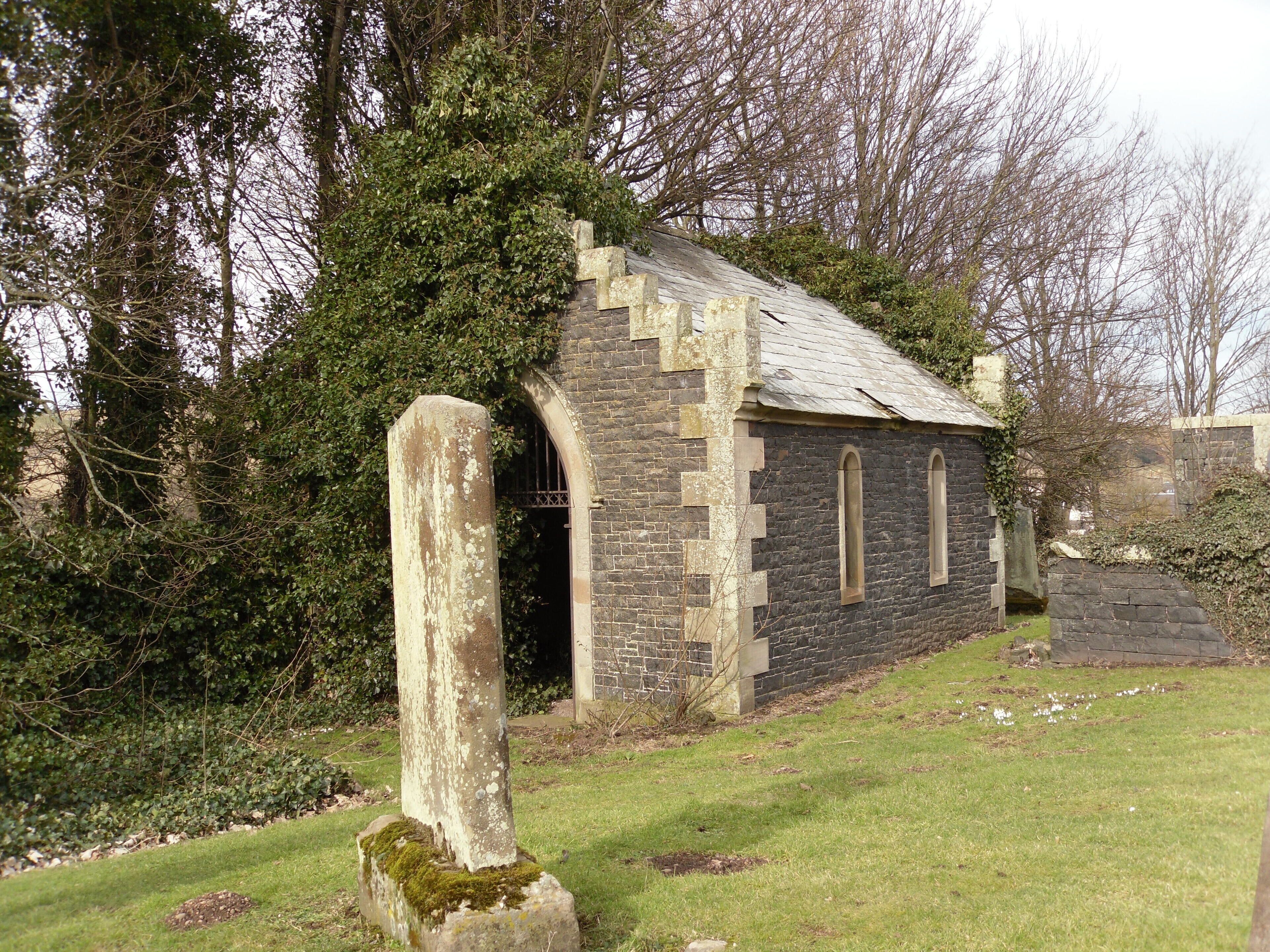 A small stone church with a moss-covered stone cross in front.