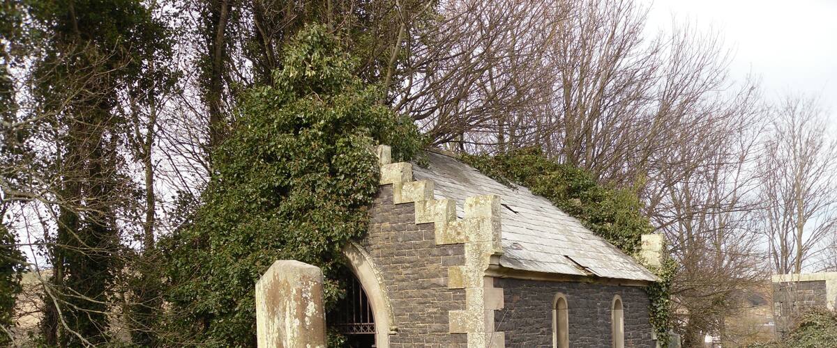 A small stone church with a moss-covered stone cross in front.