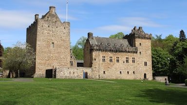 A historic stone castle with a prominent tower, surrounded by a well-maintained lawn and trees.