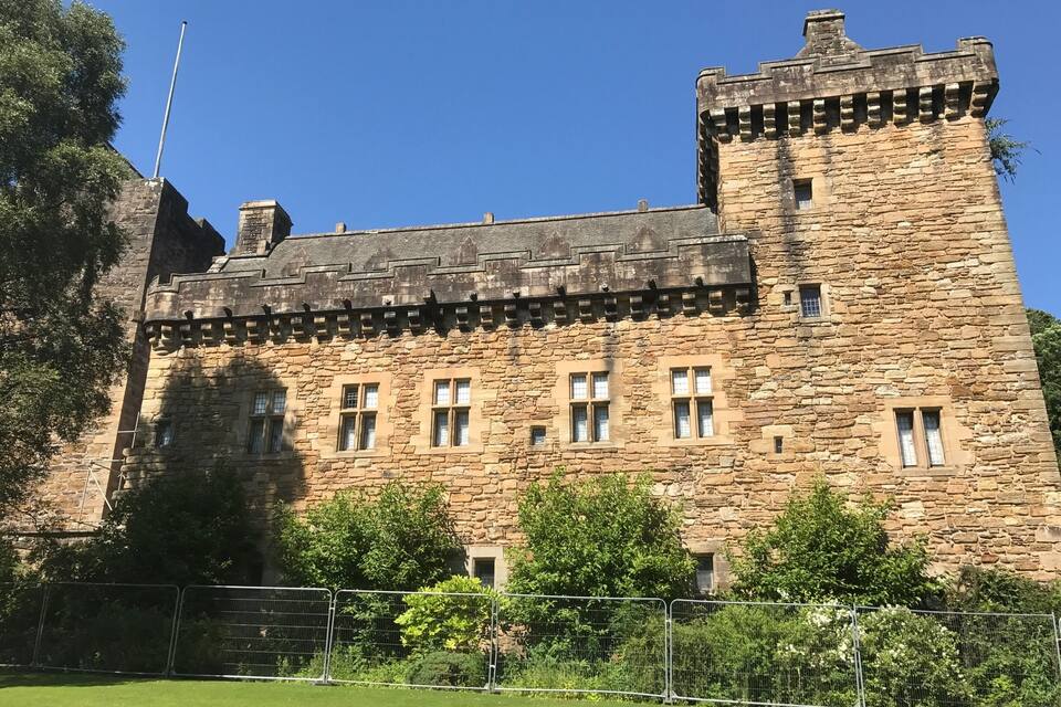 A historic stone castle with battlements, a flagpole, and a well-maintained lawn.