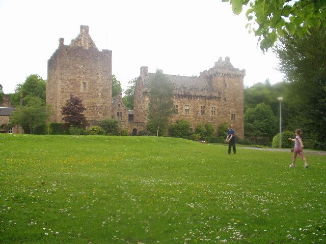 Un castillo con un campo cubierto de césped en primer plano y árboles al fondo.