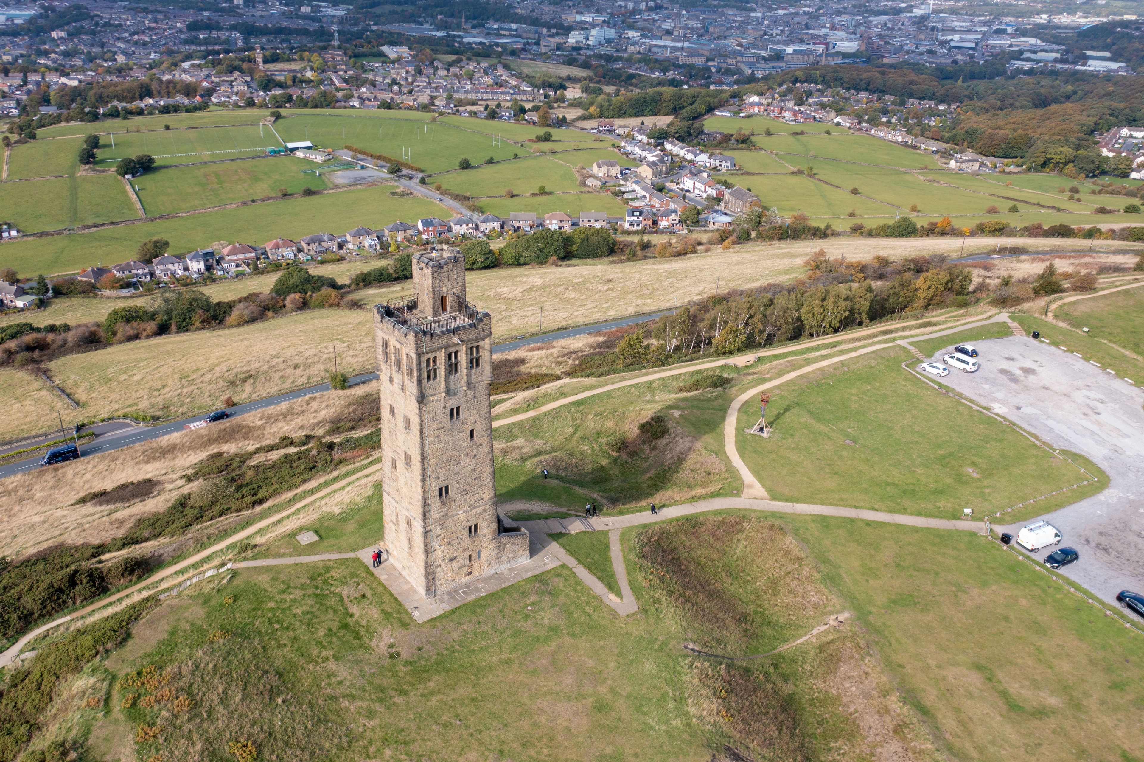 A historic tower surrounded by green fields and a small parking area.