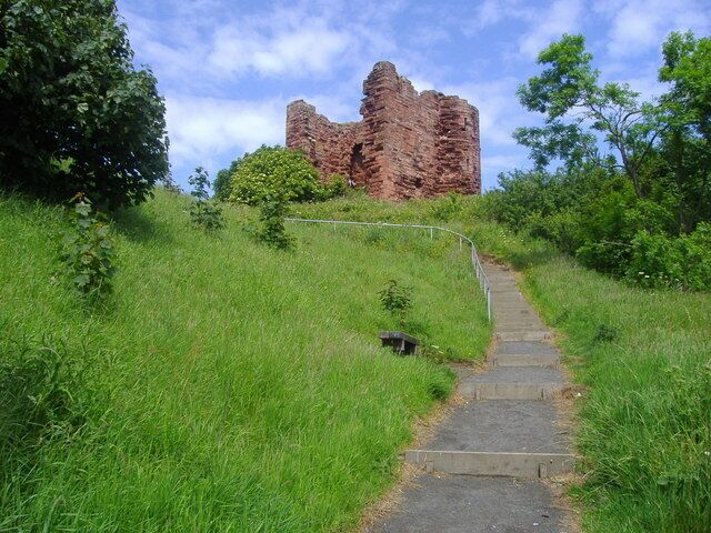 A grassy path leading to a red brick ruin with a staircase.