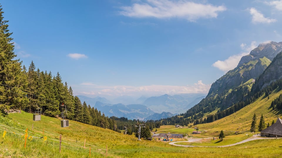 A mountainous landscape with a ski lift, a small building, and a winding road.