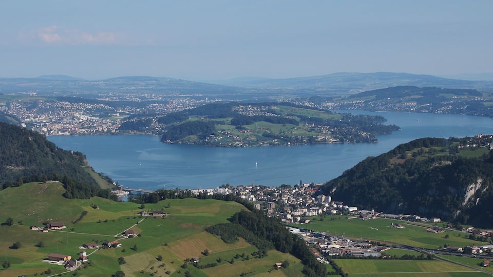 A panoramic view of a coastal town nestled between hills, with a prominent body of water and a bridge connecting the town to the mainland.