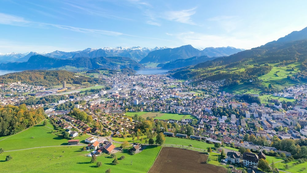 Une vue panoramique d’une ville nichée dans une vallée, avec un lac et des montagnes en arrière-plan.