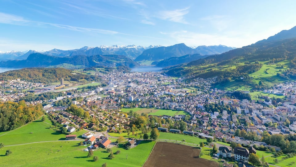 A panoramic view of a town nestled in a valley with a lake and mountains in the background.