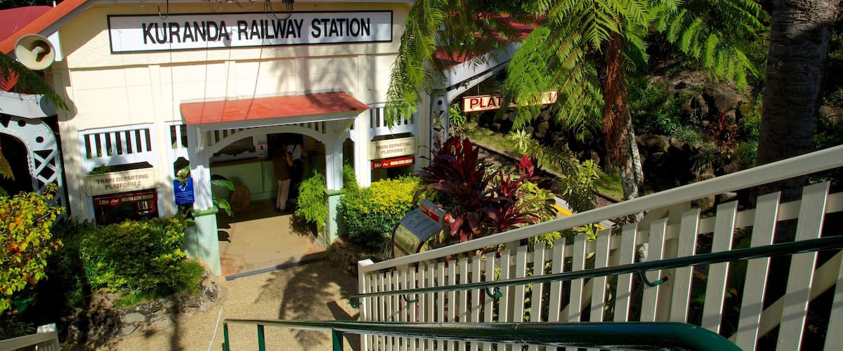 A railway station named Kuranda Railway Station with a red roof, surrounded by lush greenery and ferns.