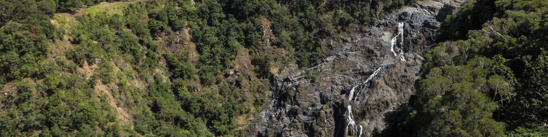 A mountainous landscape with a waterfall cascading down a rocky cliff, surrounded by dense forest.