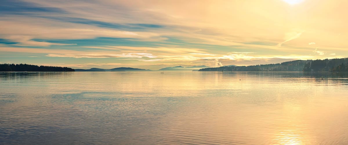 A calm lake with a forested shoreline and distant mountains.